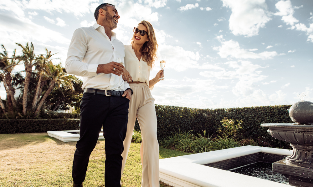 Couple walking together with wine in lawn of their house.